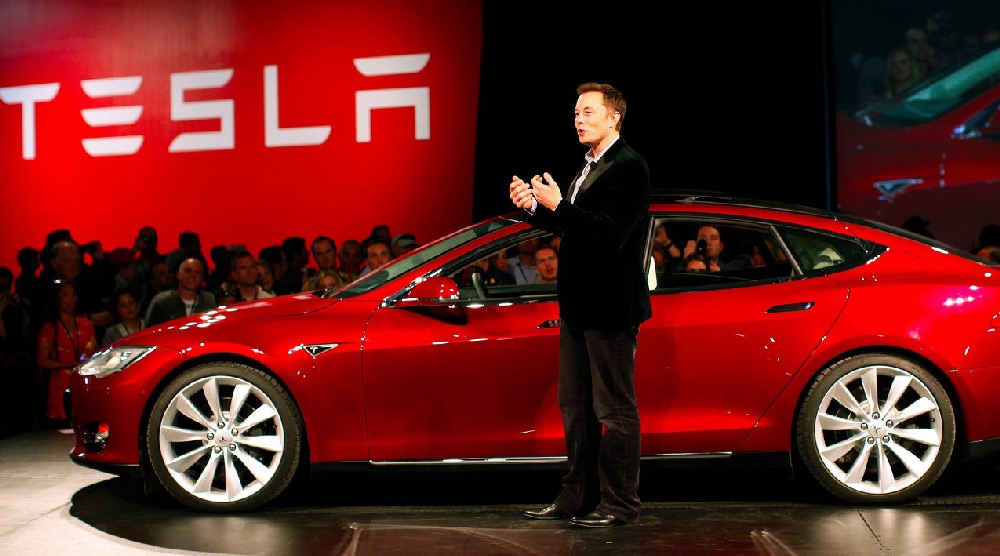 Elon Musk speaking at a Tesla event, demonstrating his role as a key figure in Tesla's marketing and brand visibility.